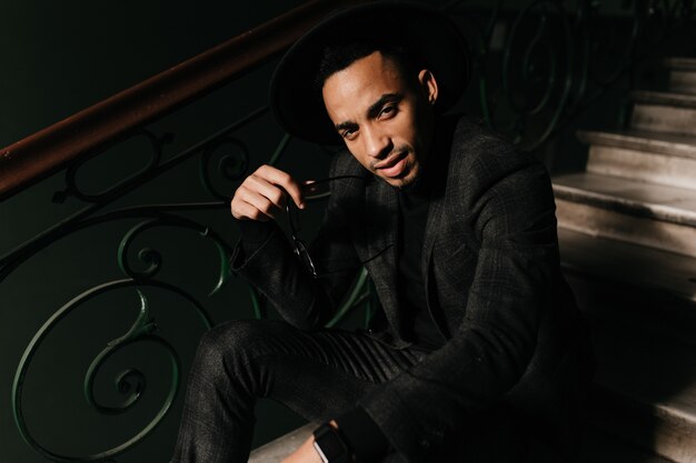 Good-looking african man sitting on stairs and looking . Tired guy in jacket posing on steps.