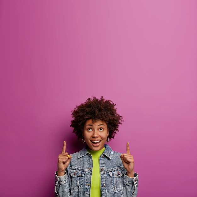 Good looking afro-american woman points above with both index fingers