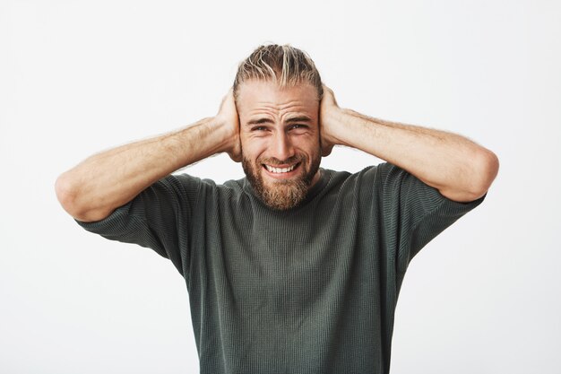 Good-looking bearded guy with stylish hairstyle close ears with hands