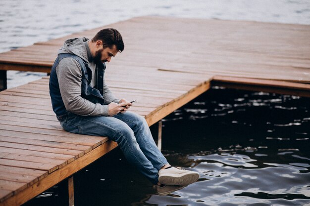 Good looking bearded man by the river in park sitting on dock