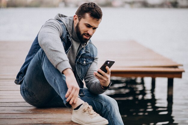 Good looking bearded man by the river in park sitting on dock