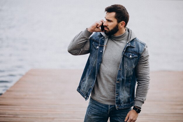 Good looking bearded man by the river in park using phone