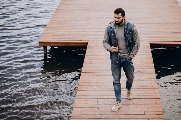 Free photo good looking bearded man drinking coffee by the river in park