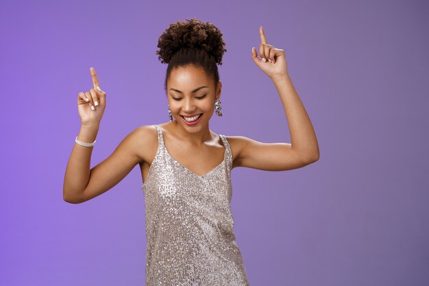 Good-looking carefree african-american girl student have fun prom dancing night club smiling delighted raicing index fingers up joyfully look down, triumphing celebrating good news, blue background.