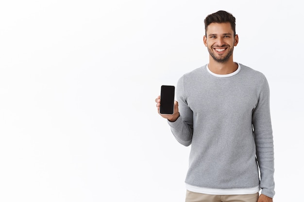 Good-looking cheerful young man promote smartphone application, holding telephone or something on mobile screen, smiling satisfied