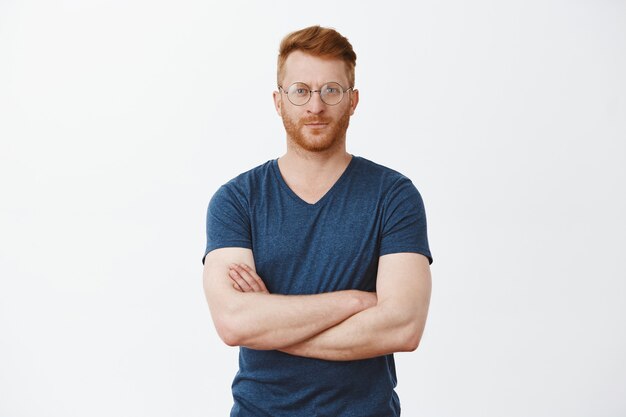 Good-looking european businessman with ginger hair and bristle in cool transparent glasses, crossing fingers on chest