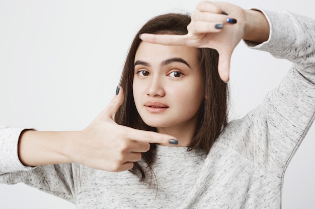 Free photo good-looking european model, lifting her eyebrow and showing frame gesture