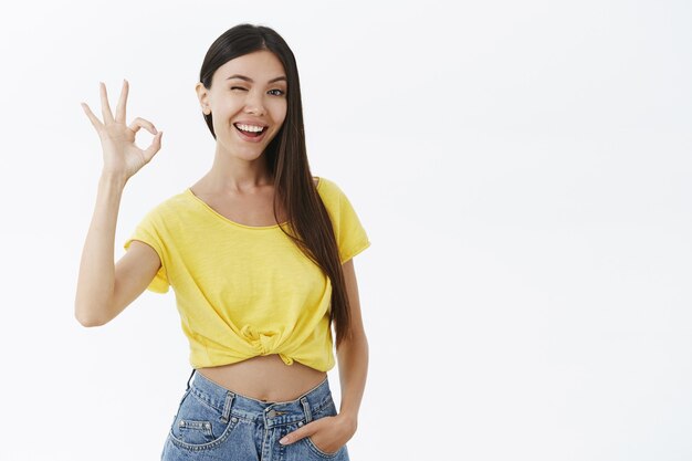 Good-looking female fitness trainer assuring she will help winking joyfully showing okay or excellent gesture with raised fingers