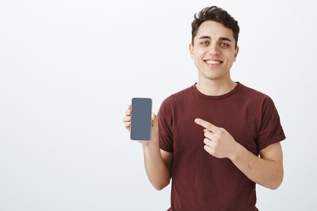 Good-looking friendly male shop assistant in casual red t-shirt showing a new smartphone