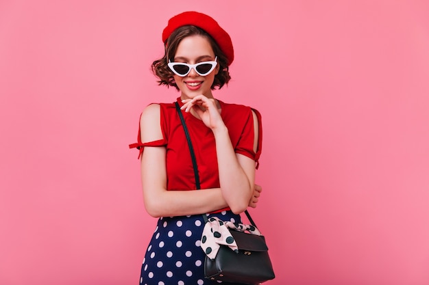 Good-looking girl in white sunglasses posing with gently smile. Beautiful dark-haired woman in french beret chilling.