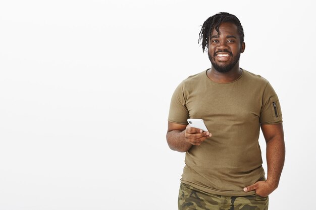 Good-looking guy in a brown t-shirt posing against the white wall with his phone