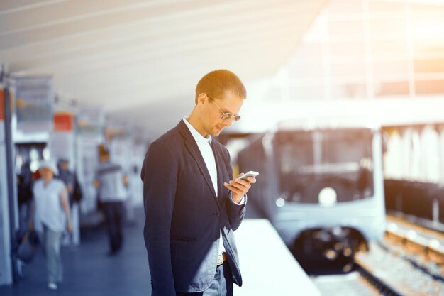 Good looking man in suit at metro station Elegant young businessman standning at metro station looking at his cell with subway train blurred in background