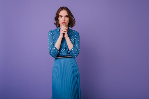 Free photo good-looking pensive girl in long skirt looking away during photoshoot. indoor portrait of concentraited brunette lady isolated on purple wall.