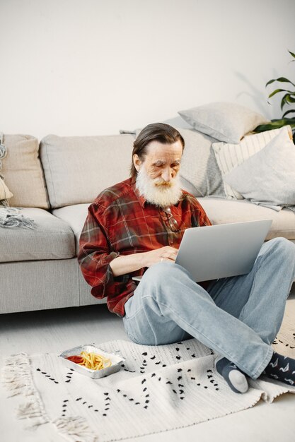 Good-looking senior man. Working with laptop. Sitting on the floor. Eating fast food.