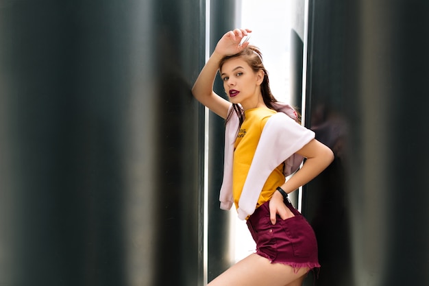 Good-looking shapely girl in trendy purple shorts posing with hand up looking with interest and mouth open