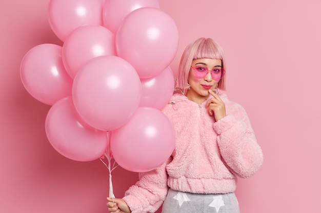 좋은 찾고 세련된 아시아 여자는 프린지 유행 선글라스 모피 코트와 핑크색 가발을 착용 암탉 파티 포즈 실내에 대한 준비 헬륨 풍선의 무리를 보유