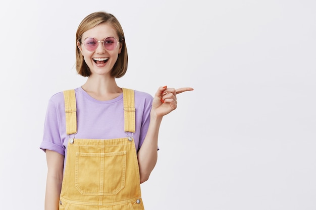 Good-looking stylish young woman in sunglasses smiling, recommend promo, pointing finger right