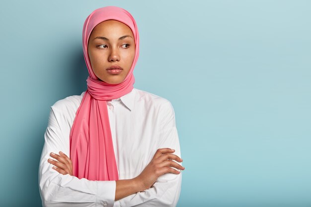 Good looking thoughtful female with dark skin, contemplates about something, keeps hands crossed