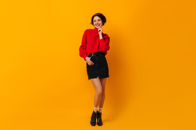 Good-looking woman in red sweater standing on yellow wall