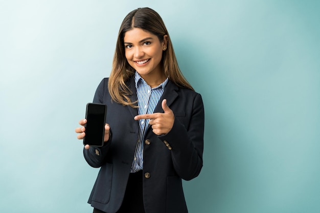 Good looking young female executive pointing at mobile phone while standing at studio