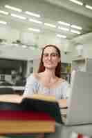 Free photo good mood. young smart long-haired woman in glasses in blouse with bare shoulders working at table with laptop looking at camera in lighted room