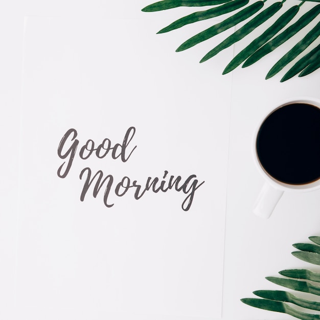 Free Photo good morning text on paper with coffee cup and leaves against white background
