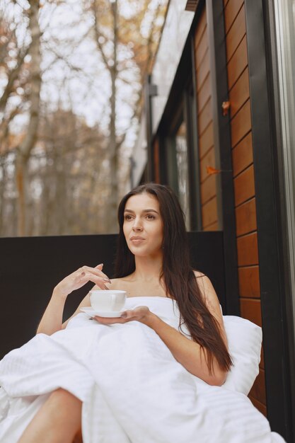 おはようございます。毛布の中の女性。テラスに座っている女性。ブルネットはコーヒーを飲みます。