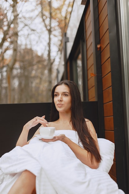 Good morning. Woman in a blanket. Lady sitting on terrace. Brunette drinks a coffee.
