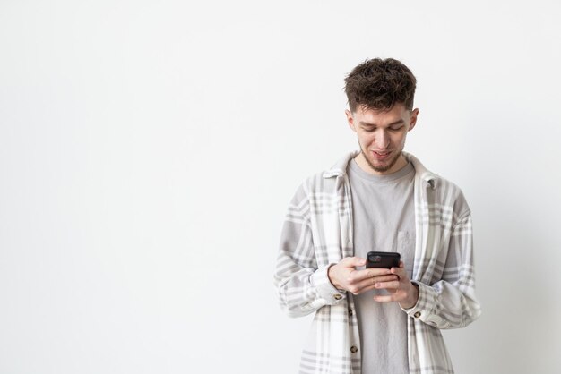 Free photo good news from friend confident young handsome man in jeans shirt holding smart phone and looking at it with smile while standing against white background