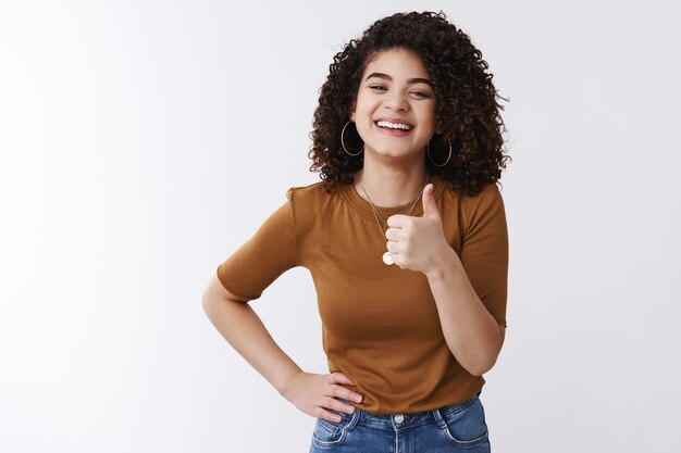 Good thanks. Happy charismatic laughing young attractive girl curly dark hair show thumb up smiling satisfied approve awesome great deal like cool choice picking outfit friend date, white background