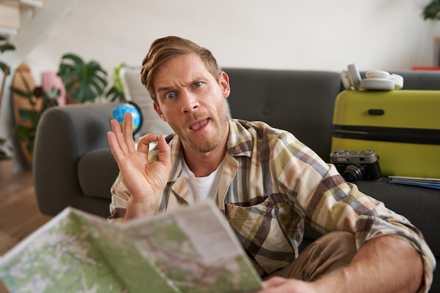 Free photo goodlooking guy tourist with travel map shows okay ok sign approve route or holiday destination