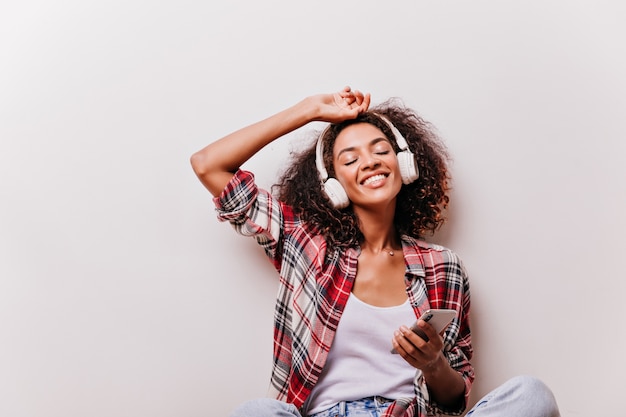 Splendida ragazza africana che tiene smartphone e ascolto di musica. affascinante modello femminile che gode della canzone con gli occhi chiusi.