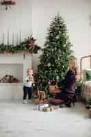 Free photo gorgeous blonde mother and cute son next to decorated christmas tree at home. family celebration.