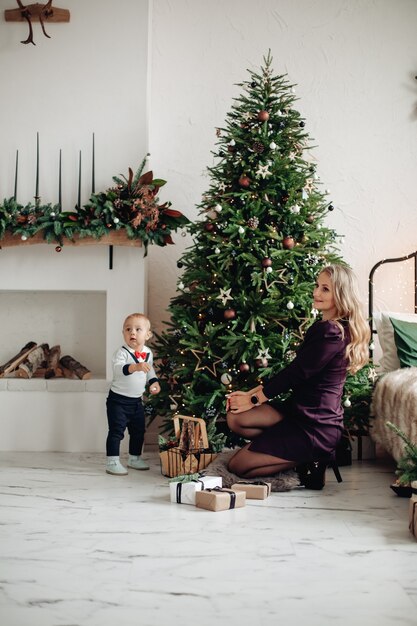 自宅で飾られたクリスマスツリーの横にあるゴージャスな金髪の母とかわいい息子。家族のお祝い。