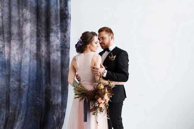 Gorgeous bride in a tender wedding dress and stylish and manly groom embrace future wife