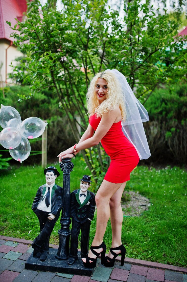 Free Photo gorgeous bride wearing red dress and veil posing outside at her bachelorette party