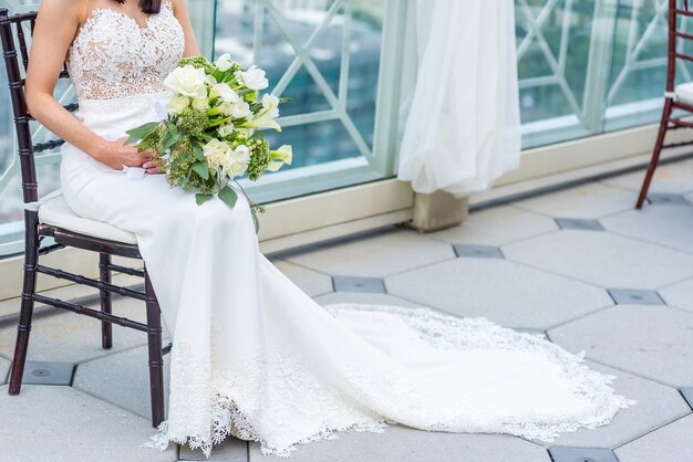 ブライダルブーケを保持している椅子に座っている豪華なウェディングドレスとゴージャスな花嫁