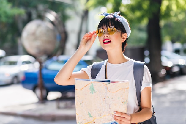 Gorgeous brunette girl in vintage outfit holding city map and looking in distance with worried face expression