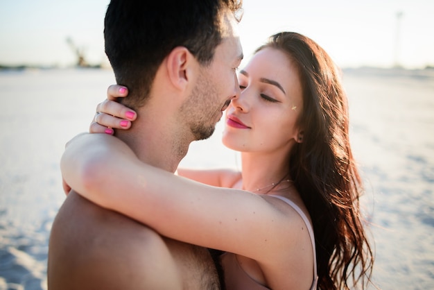 Gorgeous brunette  hugs her  man on white sand