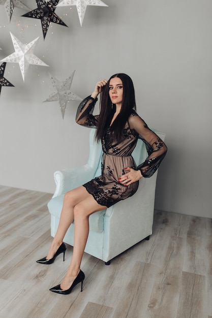 Gorgeous brunette model in black dress and heels in armchair