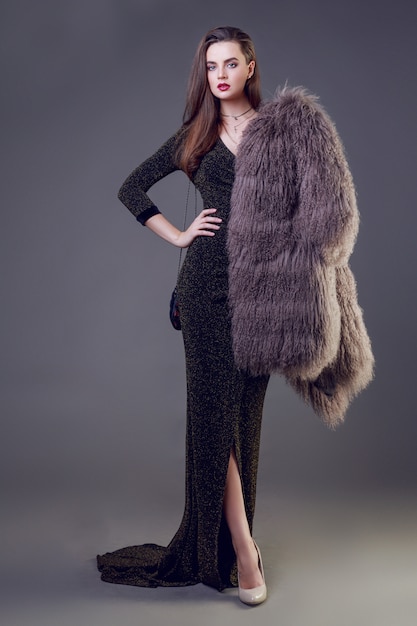 Gorgeous brunette woman with red lips wearing furry coat and cocktail dress posing