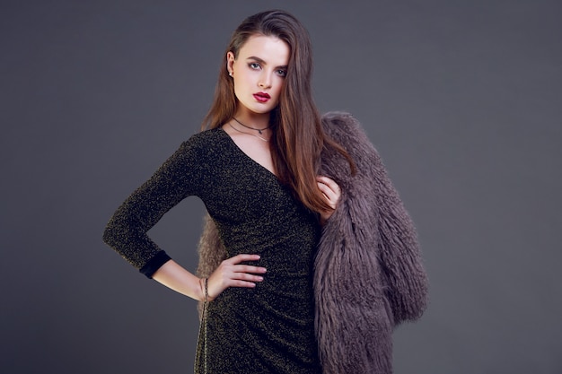 Gorgeous brunette woman with red lips wearing furry coat and cocktail dress posing