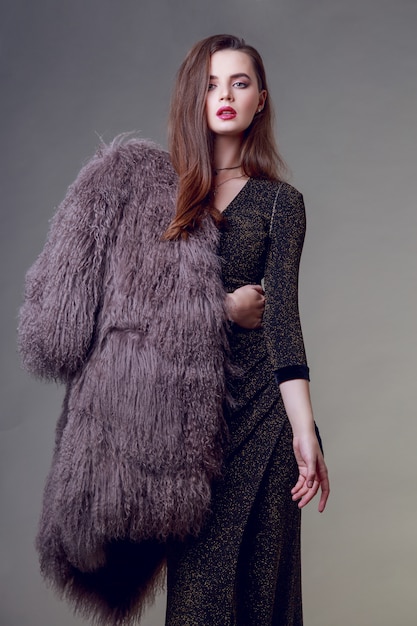 Free photo gorgeous brunette woman with red lips wearing furry coat and cocktail dress posing