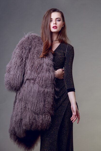 Gorgeous brunette woman with red lips wearing furry coat and cocktail dress posing