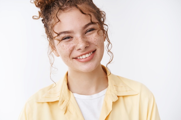 Free photo gorgeous caucasian ginger girl freckles messy curly bun tilting head friendly pleasantly smiling expressing optimism, feel happy relaxed, standing white background sharing positive memories