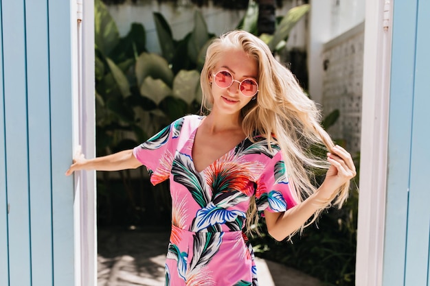 Free photo gorgeous european female model playing with her long blonde hair during outdoor photoshoot photo of graceful tanned girl in bright summer dress