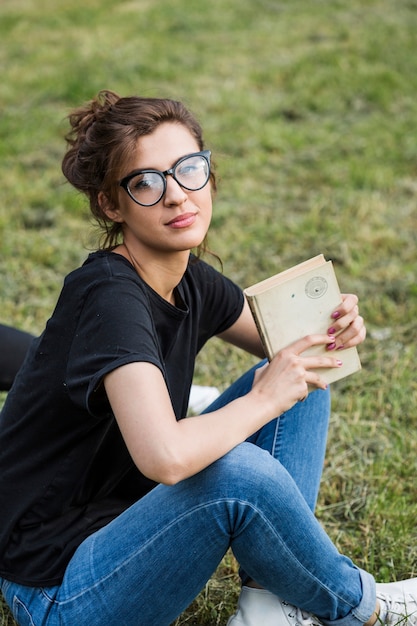 Free photo gorgeous female holding book sitting on grass