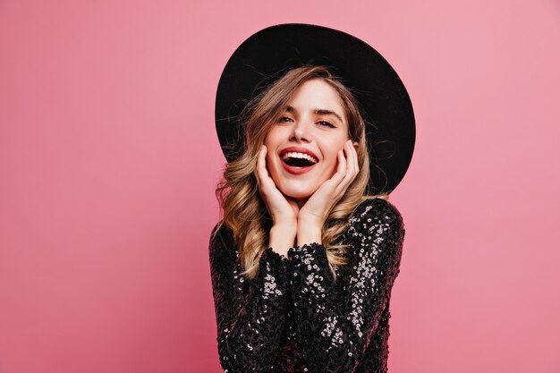 Gorgeous good-looking lady in black hat posing with excitement. Appealing white woman standing on pink wall.