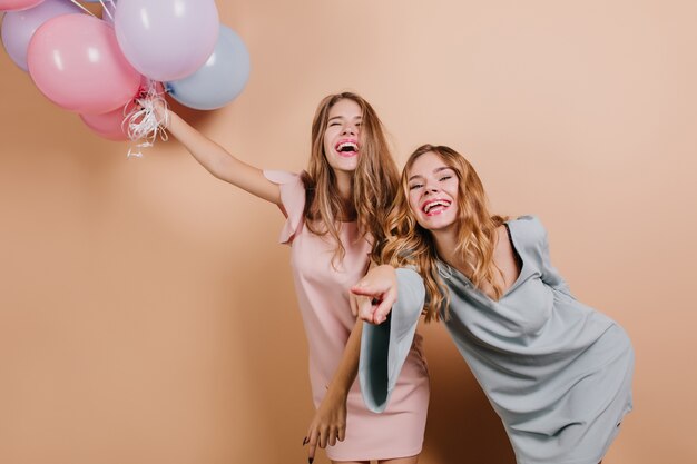 Gorgeous laughing women holding bunch of balloons with eyes closed