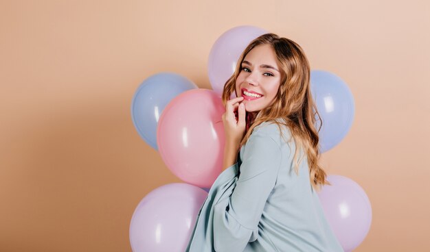 Gorgeous light-haired woman in blue attire looking over shoulder with balloons